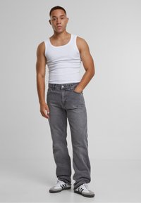 Jean en denim gris à coupe ample, avec cinq poches et fermeture par boutons. Assorti d'un débardeur blanc et de baskets noir et blanc.