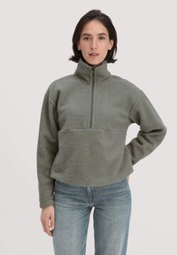 Fleece-Pullover in gedämpftem Olivgrün mit hohem Kragen, Viertel-Reißverschluss vorne und lockerer Passform. Strukturiertes Material mit Raglansäulen.
