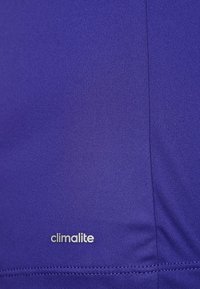 Fialová textilie s hladkou strukturou a logem "climalite". Tkanina působí lehce a má minimální detaily švů.