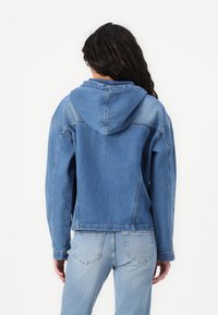 Τζάκετ τζιν με κουκούλα, ανοιχτό μπλε χρώμα, χαλαρή εφαρμογή, μακριά μανίκια, αντίθετες πάντες, ορατές ραφές και πίσω τσέπες στα τζιν.