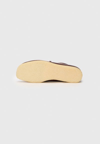 Chancla de goma marrón con una suela beige texturizada. Presenta una parte superior suave, forma redondeada y un diseño de tiras minimalista.