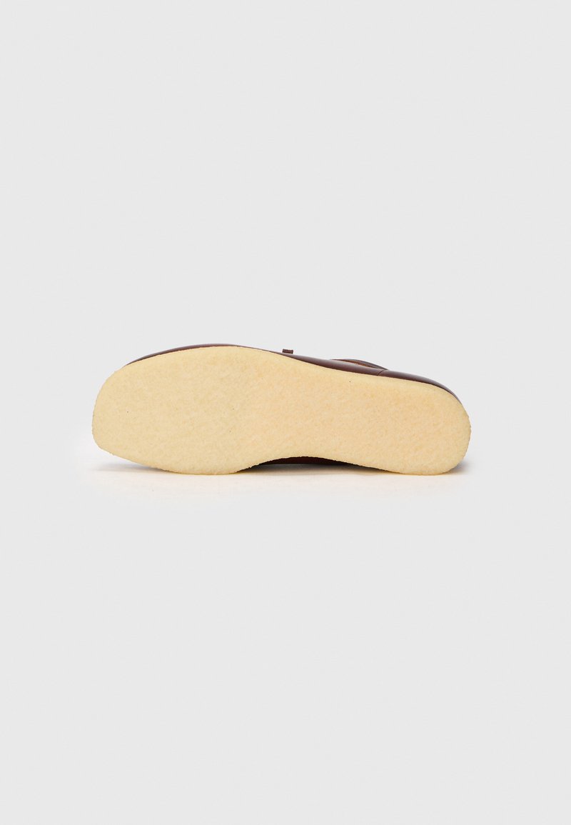 Sandale en caoutchouc marron avec une semelle beige texturée. Présente une tige lisse, une forme arrondie et un design de sangle minimaliste.