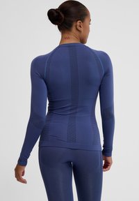 Långärmad träningströja i djupblått, med ribbat mönster och subtila vertikala linjer. Materialet verkar elastiskt och kroppsnära.