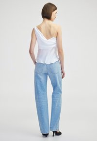 Witte satijnen cami-top met een gedrapeerde achterkant, gecombineerd met lichtblauwe jeans met witte decoratieve stiksels en een relaxte pasvorm.