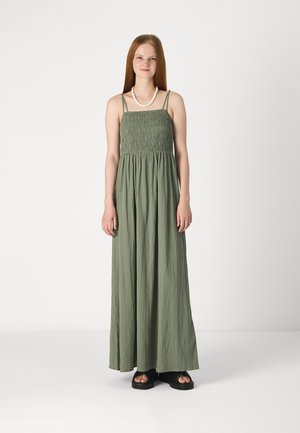 Green, sleeveless maxi dress with a smocked bodice. Features thin straps and a flowing skirt, made of lightweight fabric. Worn with black sandals.