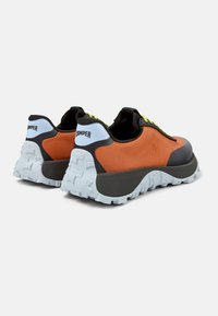 Orange and black sneakers with a textured upper, featuring a thick, white rubber sole and bright green laces. The back includes a logo.