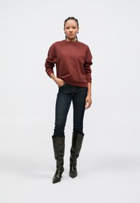 Brun genser med lange ermer, kombinert med mørke jeans og svarte støvler som går til kneet. Enkel design og avslappet passform, med ribbestrikkede mansjetter.