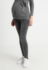 Sweater gris con textura acanalada y detalle de nudo combinado con jeans skinny gris y zapatillas blancas. Textura suave, diseño ajustado y estilo informal.