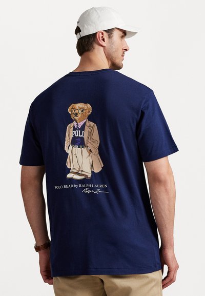 Navyblaue Baumwoll-T-Shirt mit einem Grafikdesign eines angezogenen Bären auf der Rückseite, darunter der Text "Polo Bear by Ralph Lauren" in Weiß.