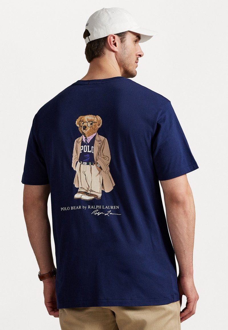 Granatowa koszulka bawełniana z grafiką ubranego niedźwiedzia na plecach, z napisem "Polo Bear by Ralph Lauren" w białym kolorze poniżej wzoru.
