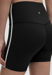 Schwarze Sportshorts mit hohem Bund, ausgestattet mit einem weißen Seitenstreifen. Glattes, dehnbares Material mit Flachnähte für zusätzlichen Komfort.