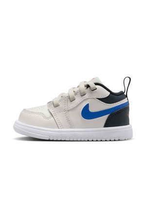 Witte peutersneaker met blauwe Nike-swoosh, zwarte hiel, witte zool en vetersluiting, zijaanzicht op een witte achtergrond.