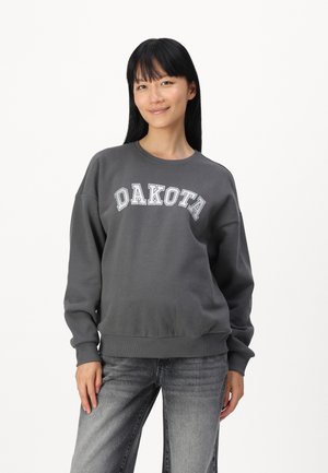 Grå hettegenser med "DAKOTA" trykt over brystet i hvitt. Har rund hals og ribbestrikkede mansjetter, laget av et mykt stoff.