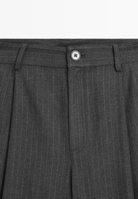 Pantalon gris foncé à fines rayures avec fermeture à boutons et passants de ceinture, montrant la ceinture avant et la partie supérieure de la cuisse.