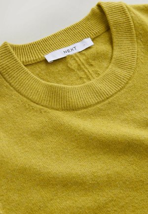 Megztinis megztas geltonos garstyčių spalvos, su ribotu apvaliu kaklu ir minkšta tekstūra. Etiketėje ant balto ženkliuko užrašyta "NEXT".