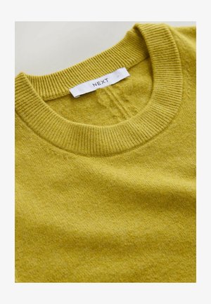 Masasoojast kollasest kootud kampsun, millel on soonikkoes ümar kaelus ja pehme tekstuur. Sildil on valgel sildil kiri "NEXT".