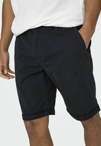 Pantalones cortos de algodón azul marino oscuro con dobladillos enrollados, bolsillos laterales y un frente plano. Presentan un lazo para cinturón tejido y una textura suave.