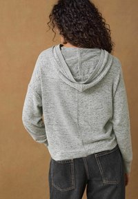 Grå hætte sweatshirt med en tekstureret overflade, der har en kengurulomme, faldende skuldre og ribbede manchetter, kombineret med mørke jeans.