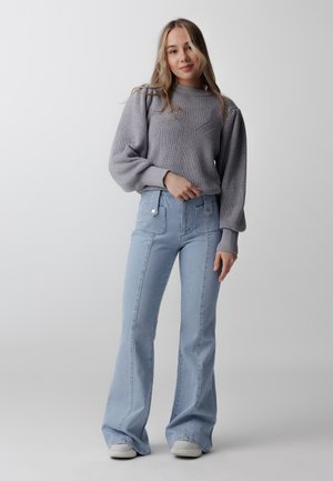 Un pull en tricot gris avec une texture côtelée et des manches bouffantes, associé à un jean évasé bleu clair avec des poches avant et une taille haute.