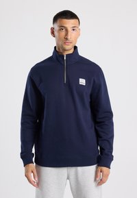 Navy blue sweatshirt with a quarter zip, ribbed cuffs, and a small white "BROOKLYN" logo patch on the left chest. Soft fabric.