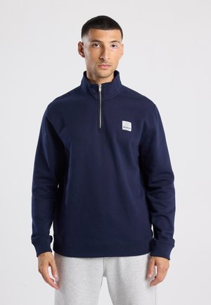 Marineblaues Sweatshirt mit einem Viertelreißverschluss, gerippten Bündchen und einem kleinen weißen "BROOKLYN"-Logopatch auf der linken Brust. Weicher Stoff.