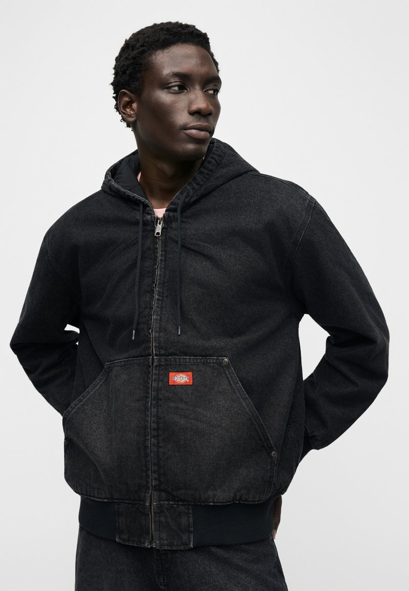 Zwarte denim hooded jas met ritsluiting, capuchon met trekkoord en een grote voorzak. Voorzien van een logo patch en geribbelde zoom en manchetten.