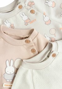 Three infant garments featuring soft fabric with pastel colors. The beige has a bunny pattern, the pink includes a bunny graphic, and the white has stripes.