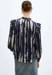 Blusa blu navy con motivo tie-dye e strisce color beige chiaro, spalle arricciate e maniche lunghe. Tessuto liscio con un drappeggio fluido.