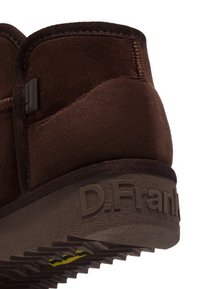 Botín de ante marrón hasta el tobillo con una superficie texturizada, que presenta un logotipo en el talón y una suela de goma texturizada con acentos amarillos.