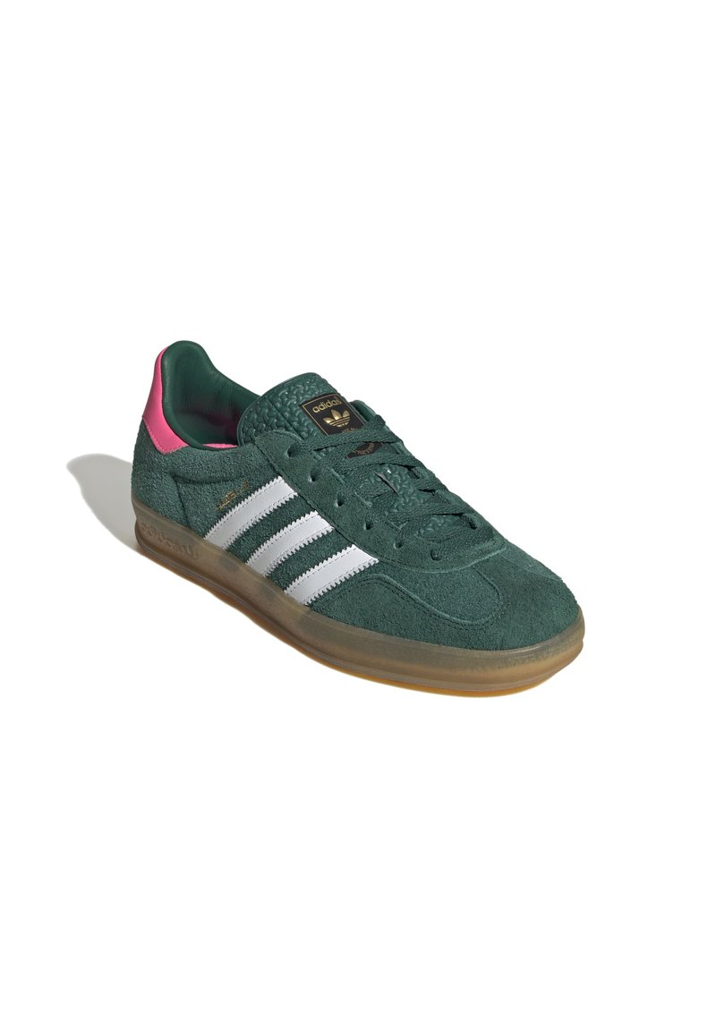 Sneaker verde in suede con strisce bianche, dettagli rosa, linguetta testurizzata e suola in gomma. Presenta un design con laccio e logo sulla linguetta.