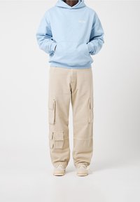 Jasnoniebieska bluza z kapturem z przednią kieszenią i logo, połączona z beżowymi spodniami cargo z wieloma bocznymi kieszeniami. Jasne trampki.