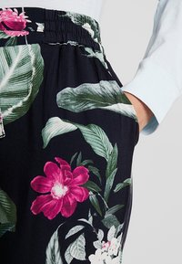 Blommönstrade byxor med svart bakgrund, livfulla rosa och gröna blad, samt en elastisk midja med sidofickor.