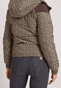 Braune gepolsterte Jacke mit geometrischem Muster. Verfügt über eine Kapuze und Rippbündchen, kombiniert mit dunklen Jeans. Signatur-Logoschild sichtbar.