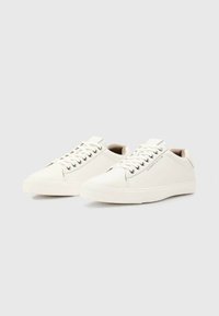 Sneakers bianchi in pelle con una texture liscia, punta arrotondata, suola piatta in gomma e occhielli metallici; design minimalista con branding sottile.