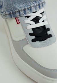 Harmaa ja valkoinen lenkkari, jossa on sileä pinta, musta ja valkoinen nauha, pehmustettu kieli ja punainen Levi's-logo.