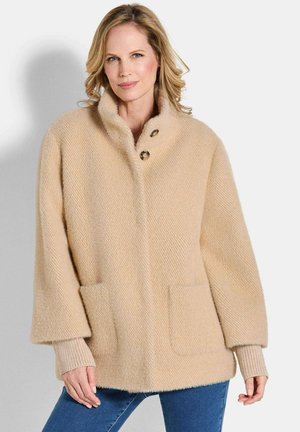 Beige herringbone jas met een oversized kraag, twee voorzakken en knoopsluiting. Zachte textuur en brede mouwen.