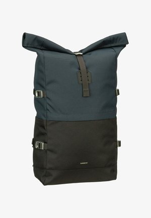 Rullemad rygsæk i mørkeblå og sort stof, med sølvhardware, side spænder og en struktureret overflade. Brandlogo foran.