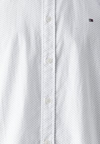 Hvid skjorte med små sorte polka-dots, med en klassisk krave og plastknapper, samt et lille logo på venstre bryst.