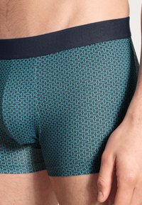 Boxershorts met een geometrisch patroon in teal en zwart, met een zachte elastische tailleband. Het materiaal lijkt glad en aansluitend.