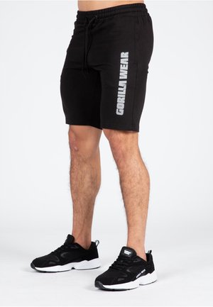 Shorts de sport noirs avec une taille élastique, des poches latérales, et le logo "GORILLA WEAR" en argent sur la jambe gauche. Portés avec des baskets noires.