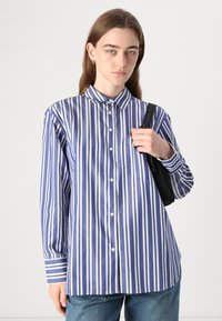 Blå- og hvitstripete langermet skjorte med krage som kan knappes, med en brystlomme og avslappet passform. Kombinert med denimbukser.