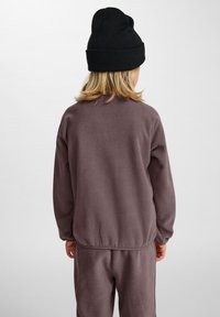 Grå fleecetröja med rundad halsringning, långa ärmar och elastisk nederkant. Svart stickad mössa. Texturen verkar mjuk och mysig.