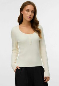 Maglietta a maniche lunghe in rilievo color crema con scollatura a barca e patta con tre bottoni, caratterizzata da una texture morbida e un design aderente.