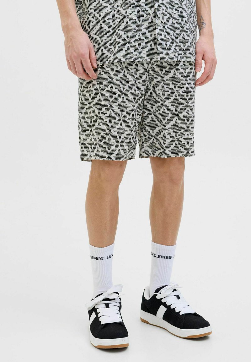Shorts à motifs en noir et blanc avec un design géométrique. Fabriqués en tissu texturé. Associés à des baskets noires et des chaussettes blanches.