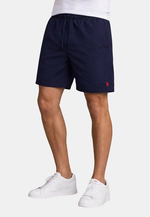 Man wearing navy blue casual shorts with elastic waistband and white sneakers, standing against a plain background.