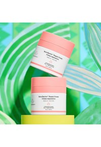 Bora Barrier™ Repair Cream in a round white container with a pink lid, featuring a printed label and a smooth surface, positioned on a yellow base.