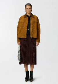 Veste en coton marron sur un top noir, associée à une jupe plissée bordeaux à pois blancs et des bottines noires. Sac à main argenté inclus.