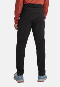 Schwarze Slim-Fit-Hosen aus strapazierfähigem Material. Mit hohem Bund und geknöpften Manschetten. Kombiniert mit hellblauen Sneakers.