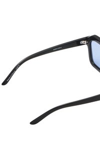 Occhiali da sole neri con lenti blu, dotati di montatura in plastica elegante e aste diritte e affusolate. Tra gli accenti c'è un piccolo snodo.