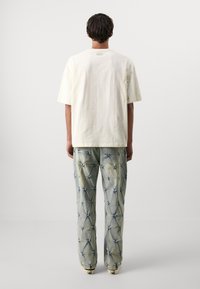 Crème katoenen t-shirt met een relaxte pasvorm, gecombineerd met blauwe spijkerbroeken met een gestikt patroon en een licht verouderde afwerking.